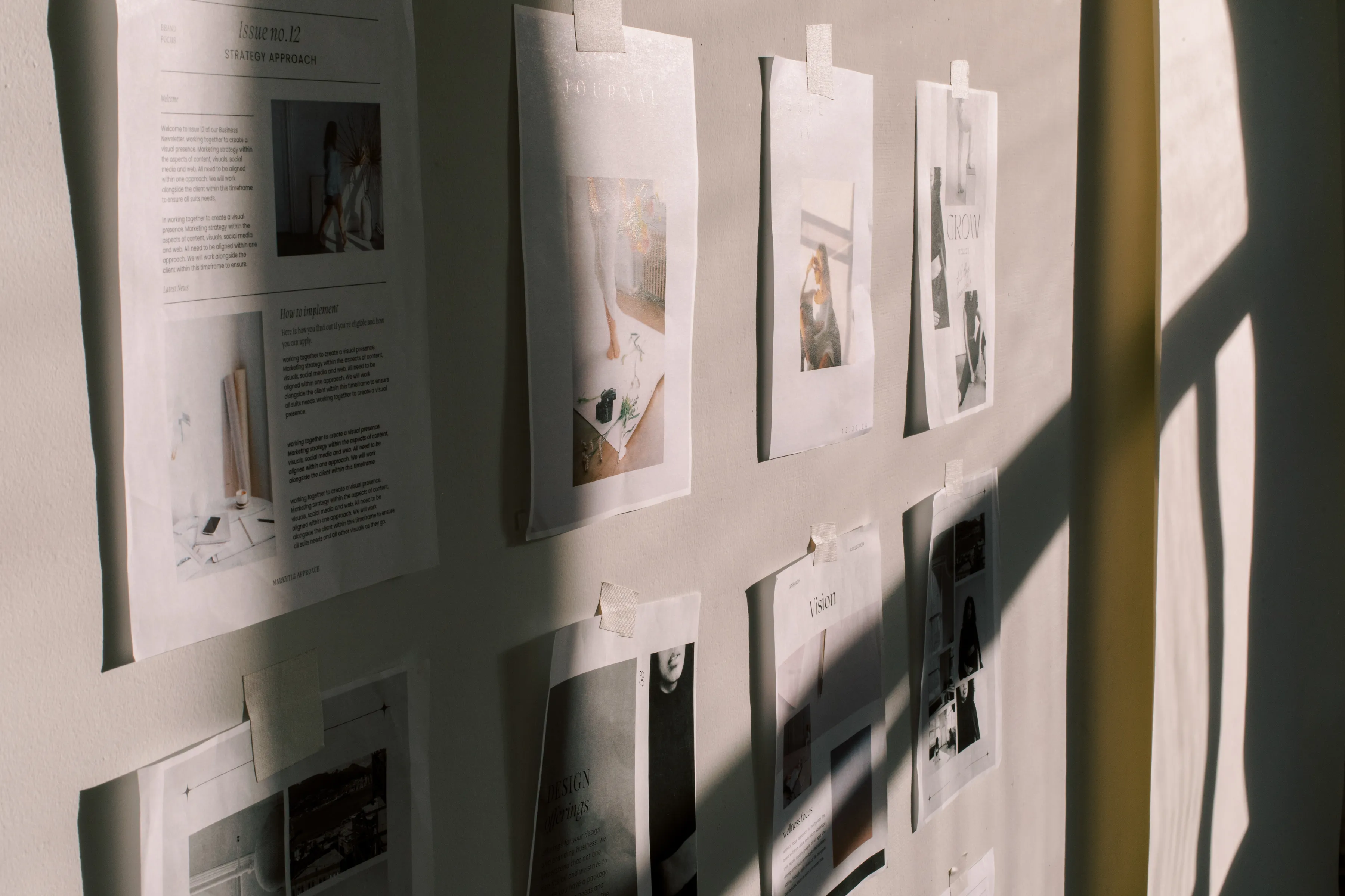 Papers pinned to a wall. There are shadows playing against the papers and it looks quite moody. There are words on the papers like strategic approach, vision and design